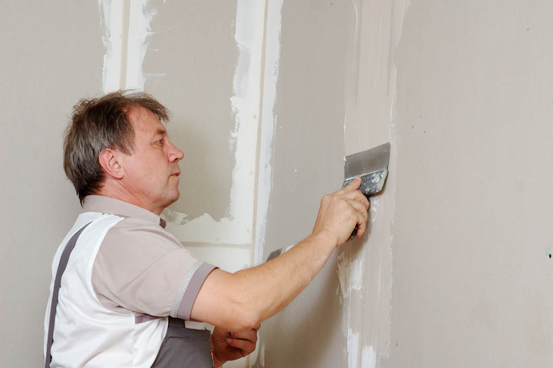 A man working on a wall with tools, wearing a vest and using a level.