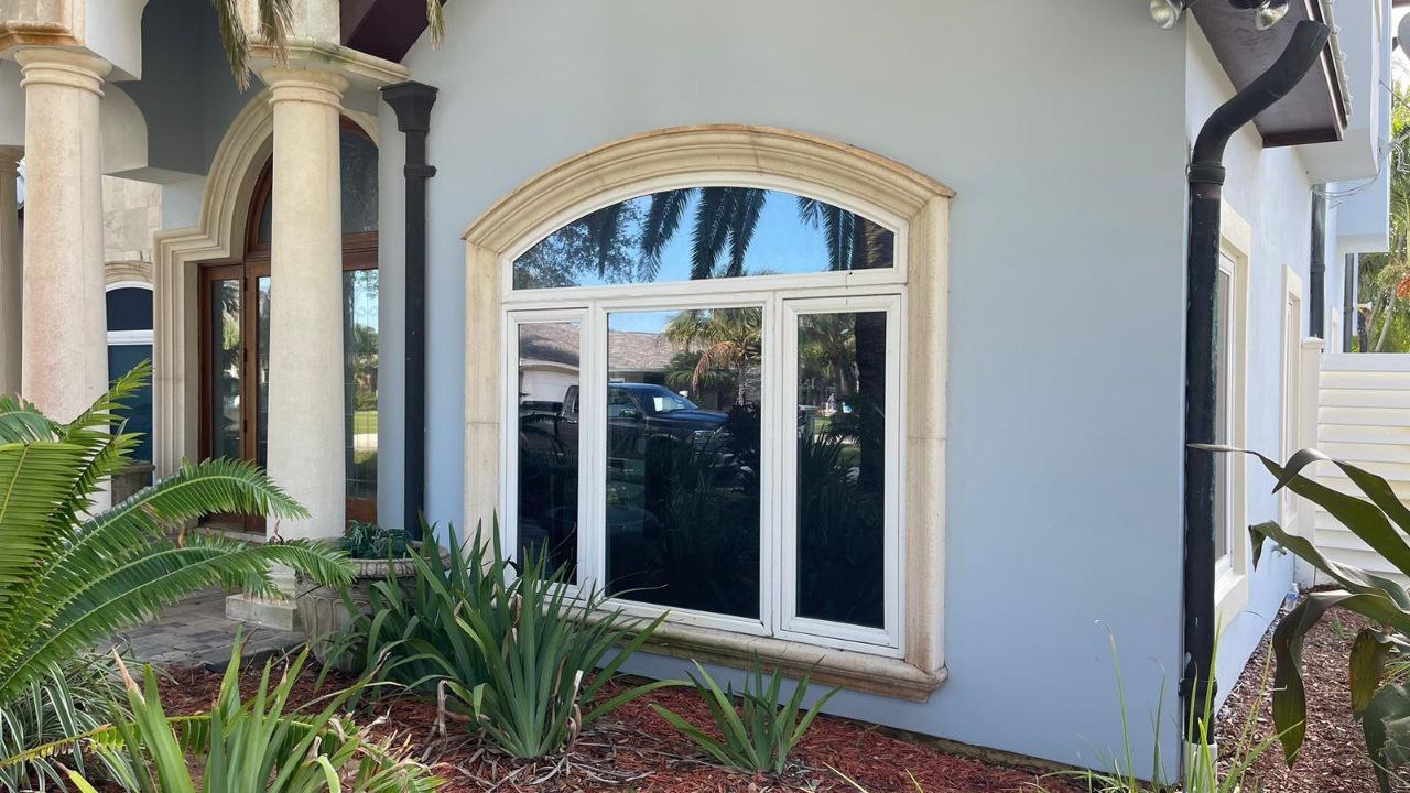 The image shows a house with a prominent arched window, a white exterior wall, and a covered porch area.