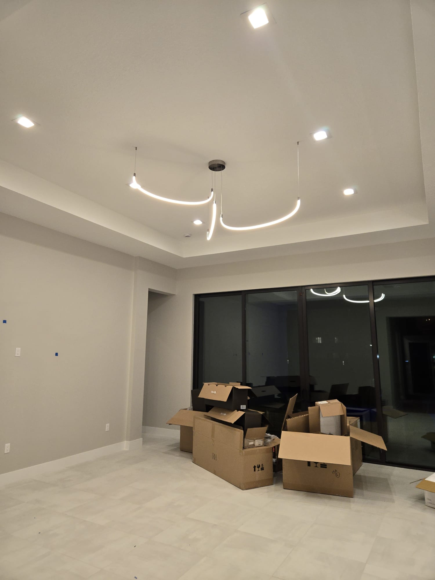 The image shows an interior space with a ceiling light fixture, boxes on the floor, and a large window allowing natural light into the room.