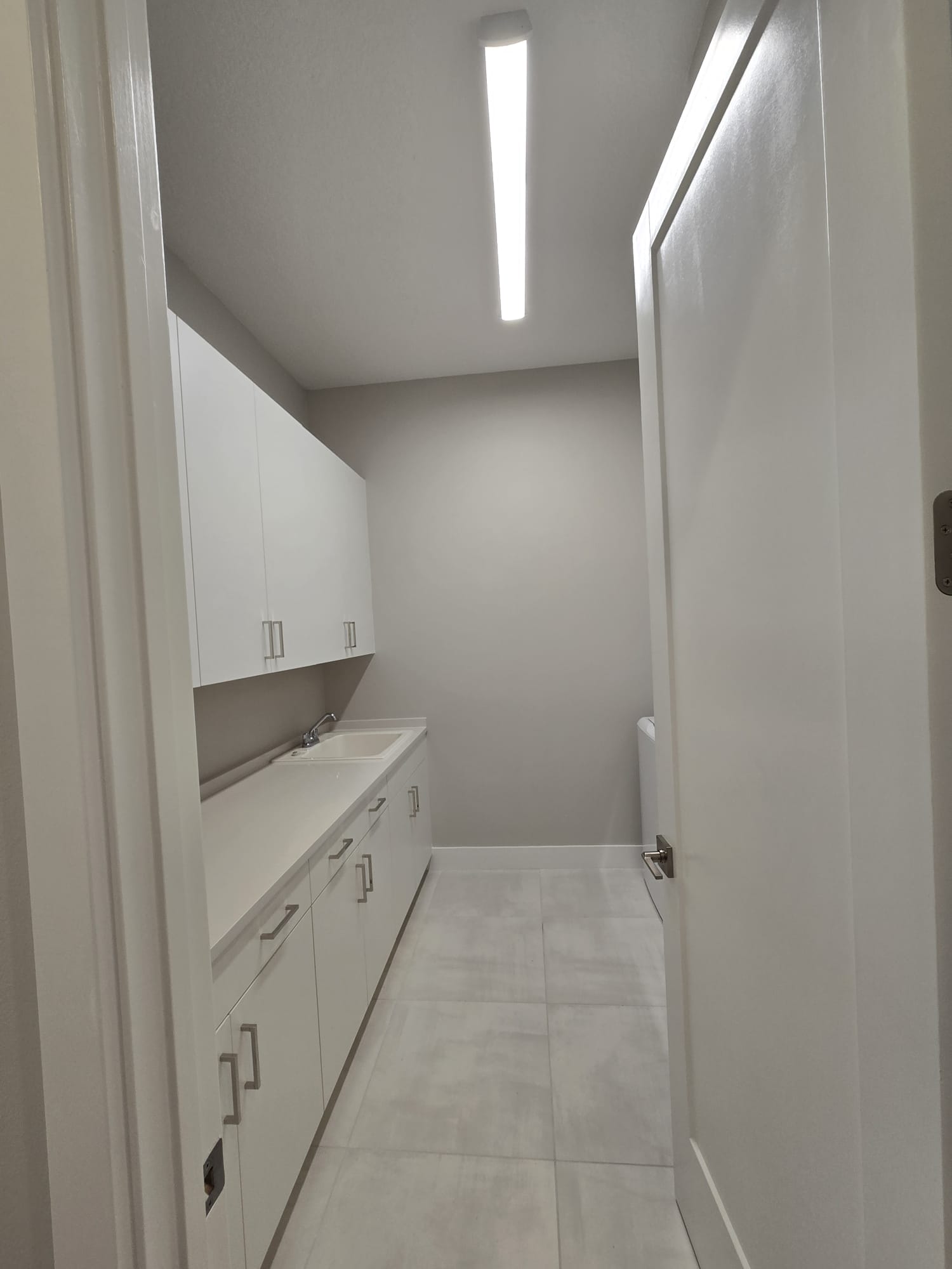 The image shows a small, empty bathroom with white walls and fixtures, featuring a toilet, sink, and cabinets.
