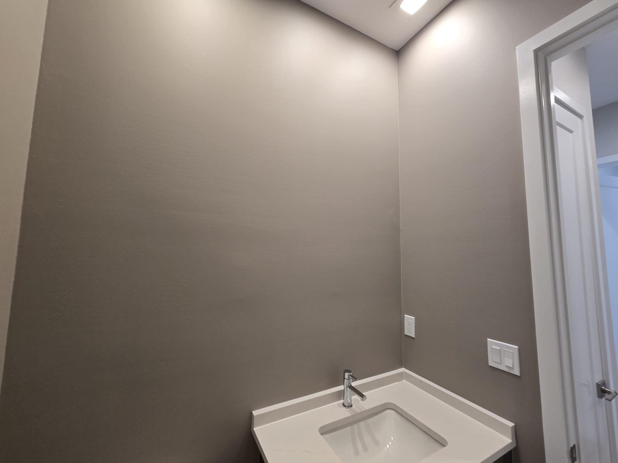 The image shows a bathroom with a brown wall, a white sink, and a dark-colored floor.