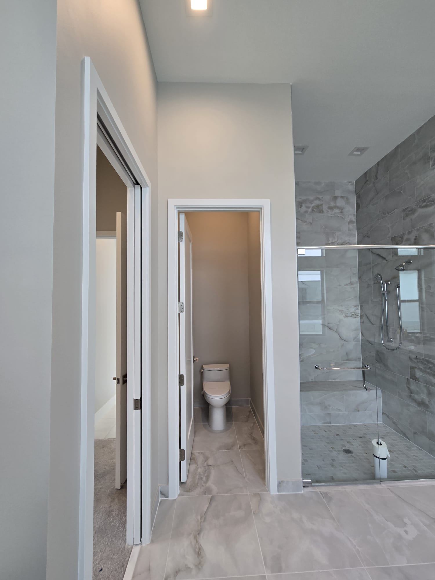 The image shows a modern bathroom interior with a shower stall on the right and a toilet on the left side of the frame, featuring tiles, a large mirror above the sink, and a clean design.