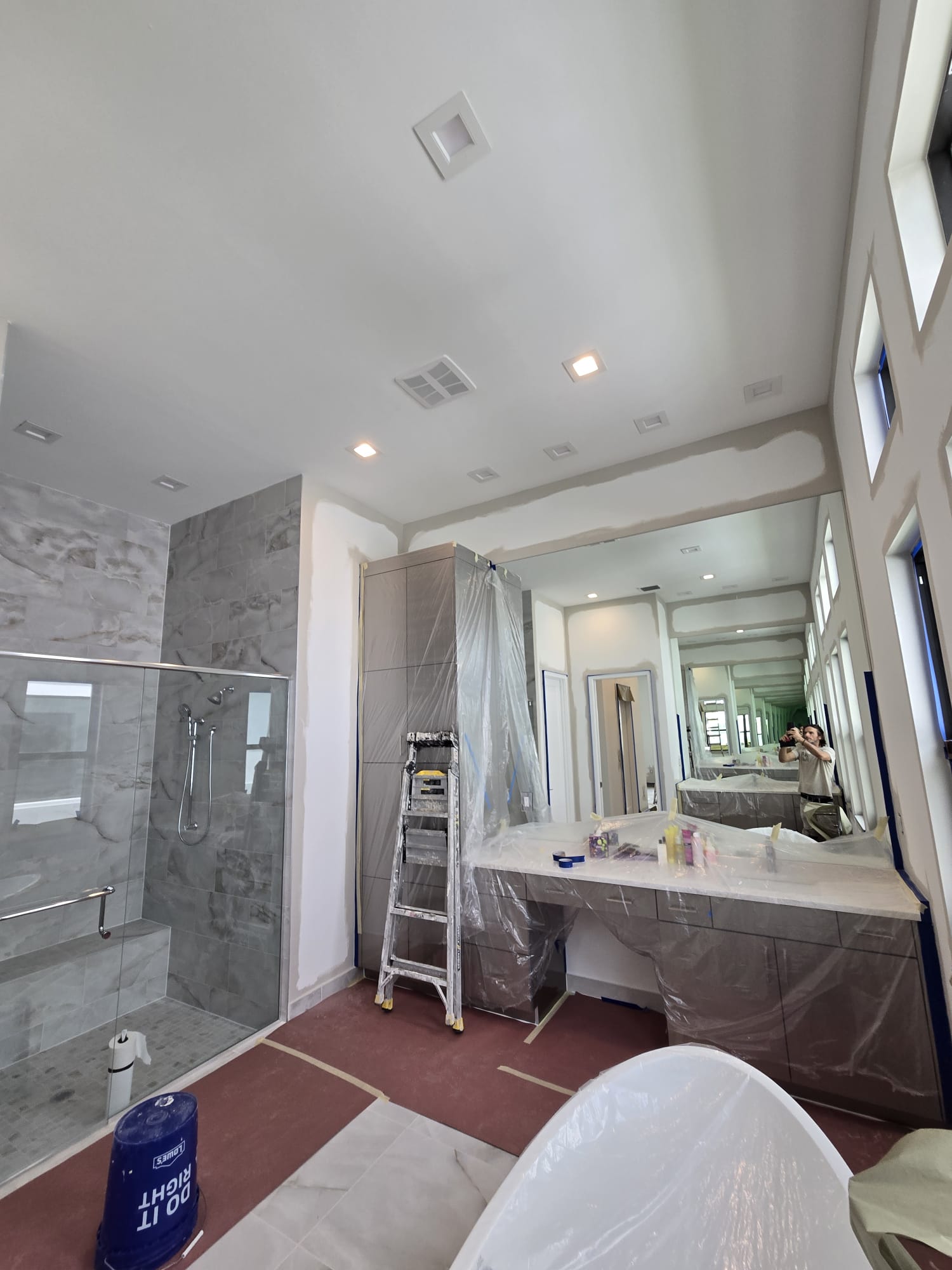The image shows a bathroom undergoing renovation with a focus on the large mirror above the sink and the partially covered fixtures.