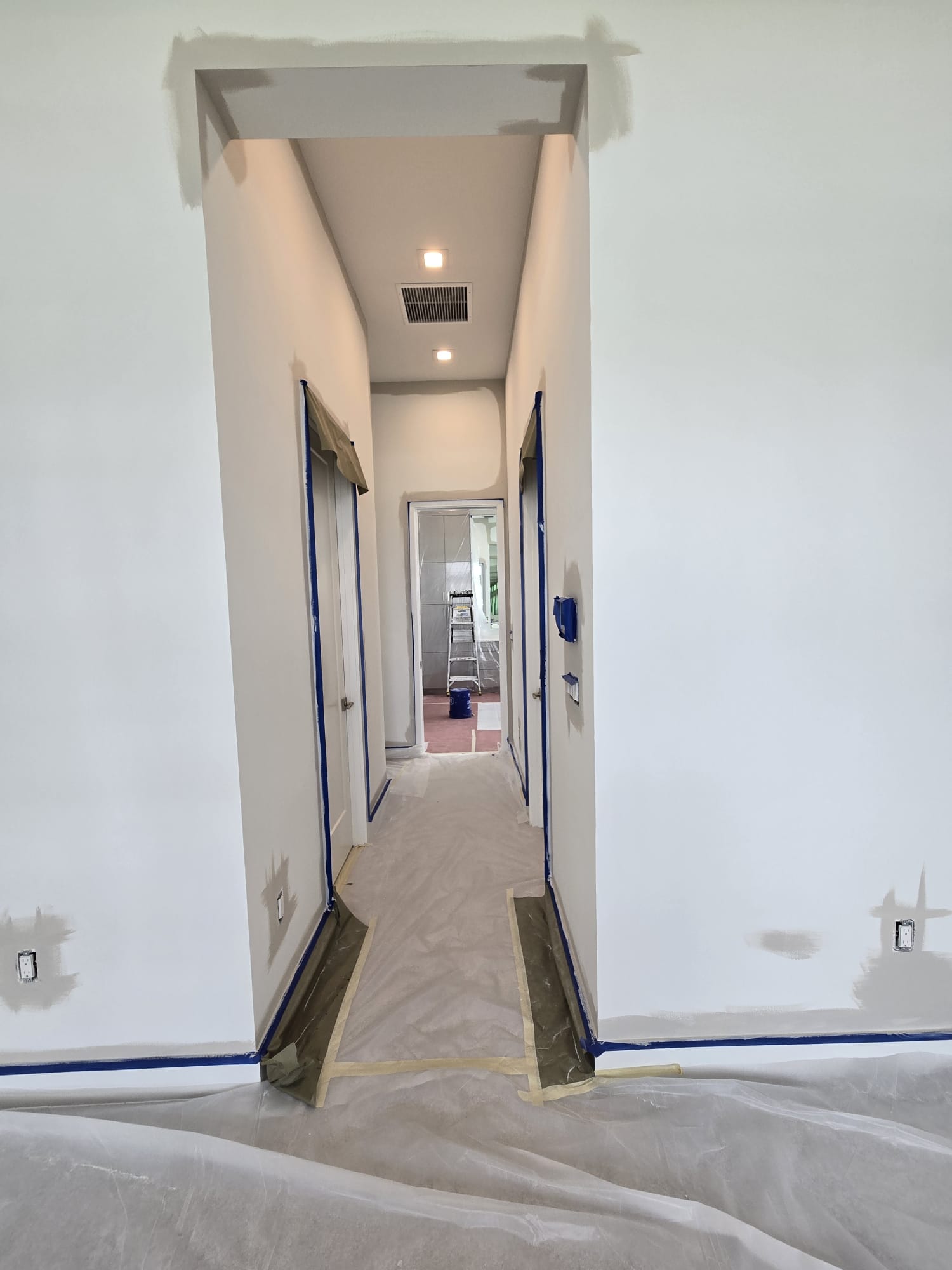 The image shows an interior hallway with a white wall on the left, a wooden floor, and a doorway leading into another room.