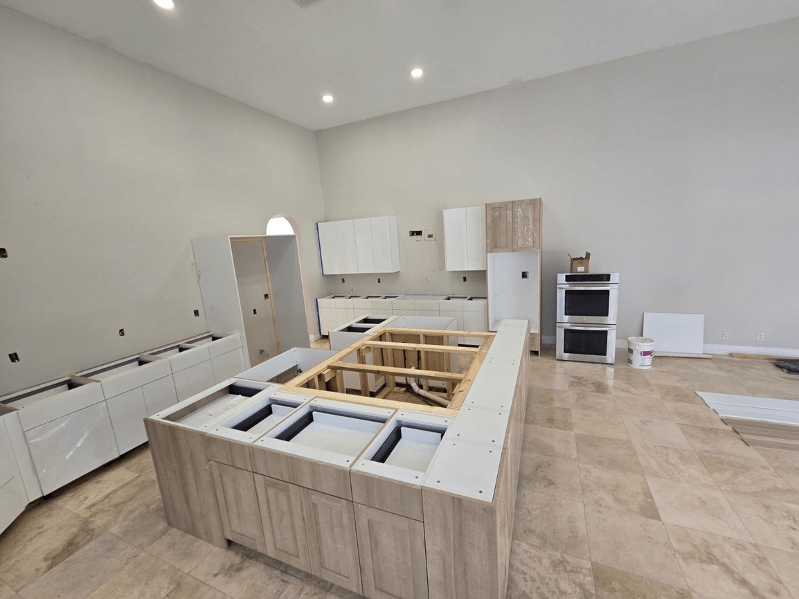 A modern kitchen with light wood cabinets, white countertops, stainless steel appliances, and a large island in the center.