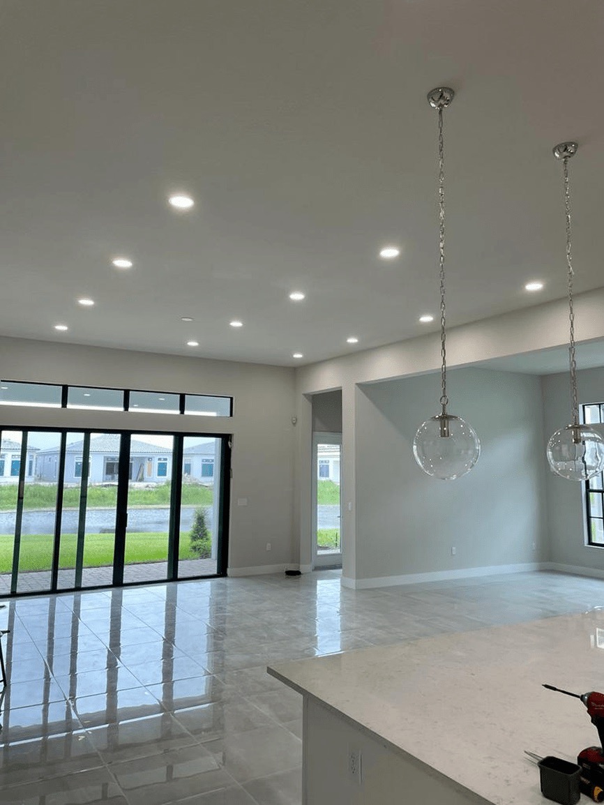 The image depicts a modern interior space with a spacious kitchen area featuring a large island countertop, stainless steel appliances, and recessed lighting.