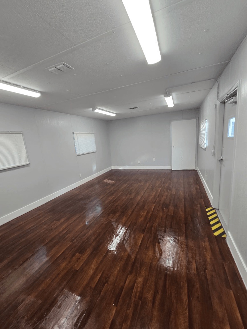 The image shows an interior space with a polished hardwood floor reflecting overhead lights, a wall-mounted air conditioning unit, and a large, open area with no visible furniture or decorations.