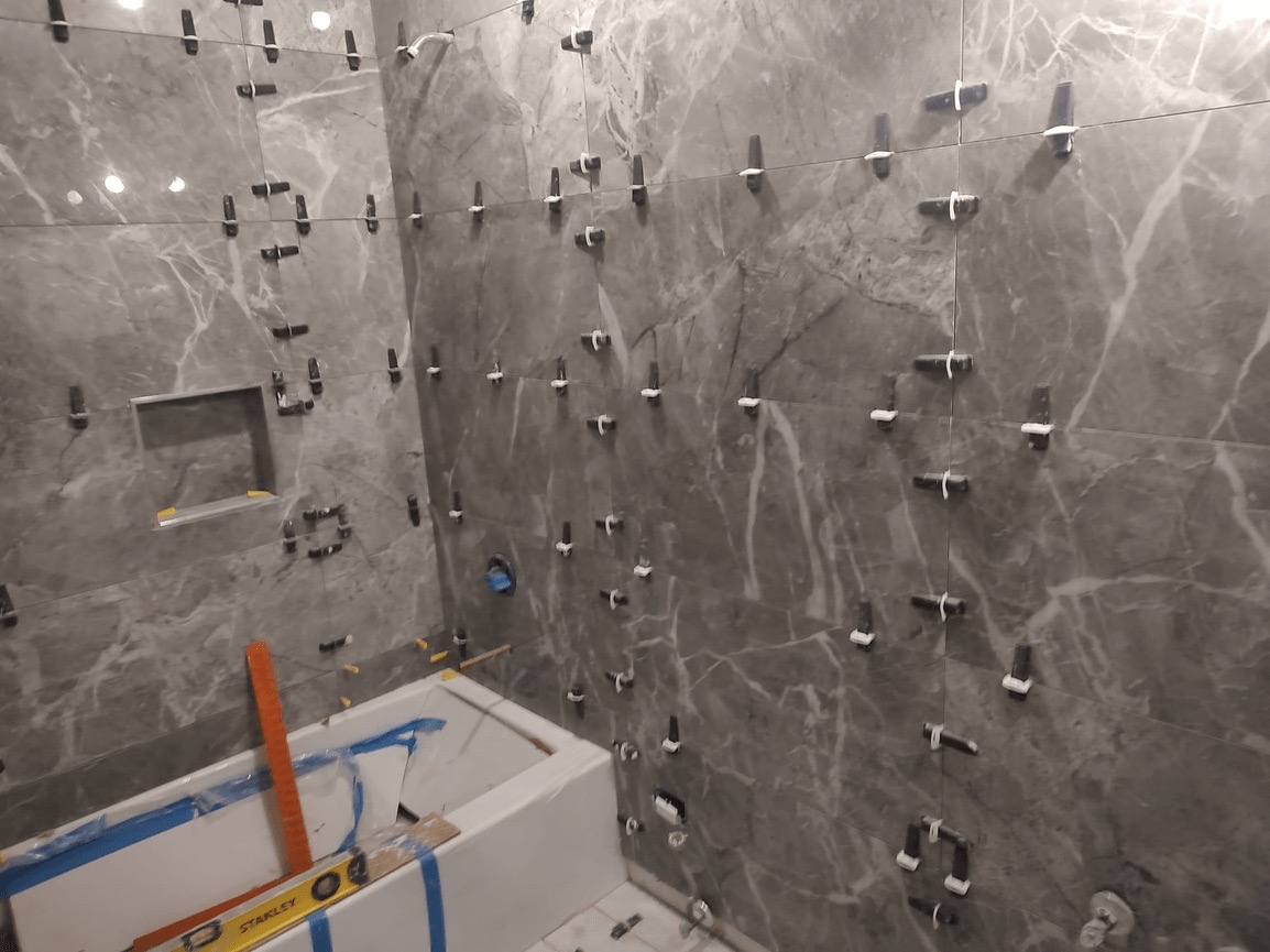 An interior view of a bathroom under renovation with marble walls, exposed fixtures, and a partially tiled floor.