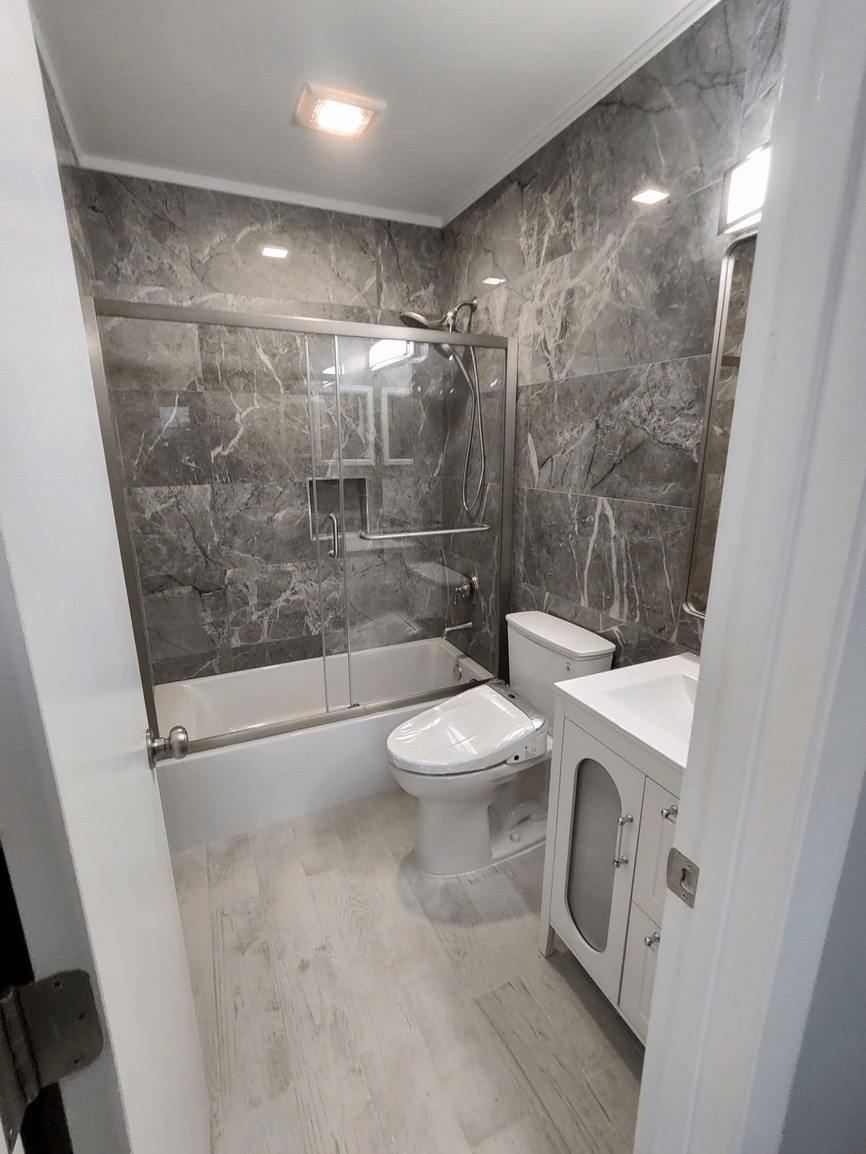 The image shows a modern bathroom with a toilet, sink, shower, and tiled walls.