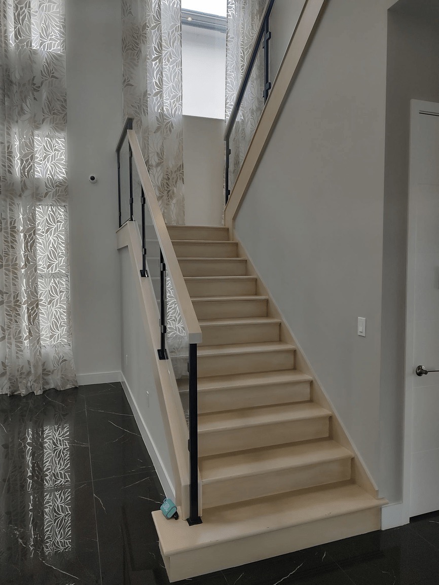 The image shows a modern interior featuring a staircase with a black handrail leading to an upper level, set against a backdrop of a wall-mounted railing and a patterned curtain.