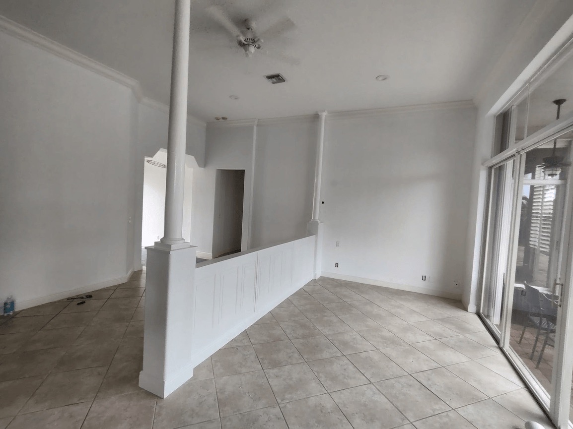 The image depicts an interior space with a white staircase leading up from a lower level to an upper level, where there are white walls and a white floor. A large window on the right side of the room allows natural light to enter the space.