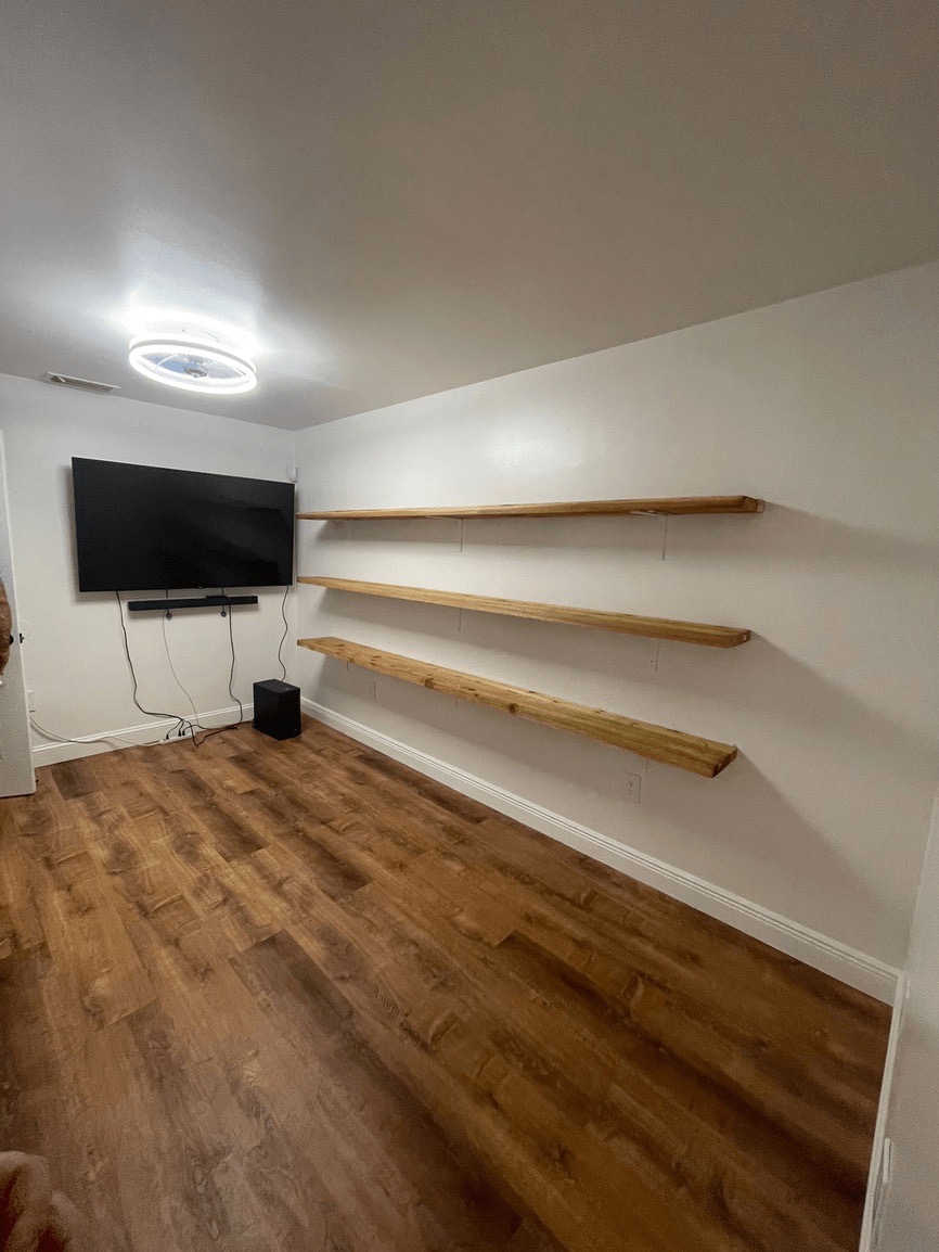 The image shows an interior space with a hardwood floor, white walls, and a large open area leading to a room with built-in shelves.
