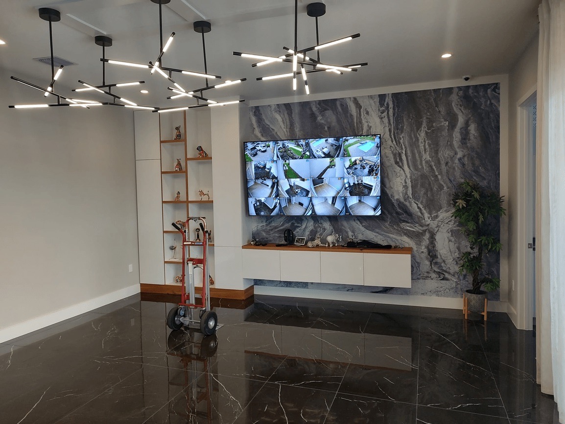 This is an interior view of a modern living room with a large flat-screen TV mounted on the wall above a wooden console table, a marble floor, a black and white geometric wallpaper design, a ceiling light fixture, and a contemporary decor style.