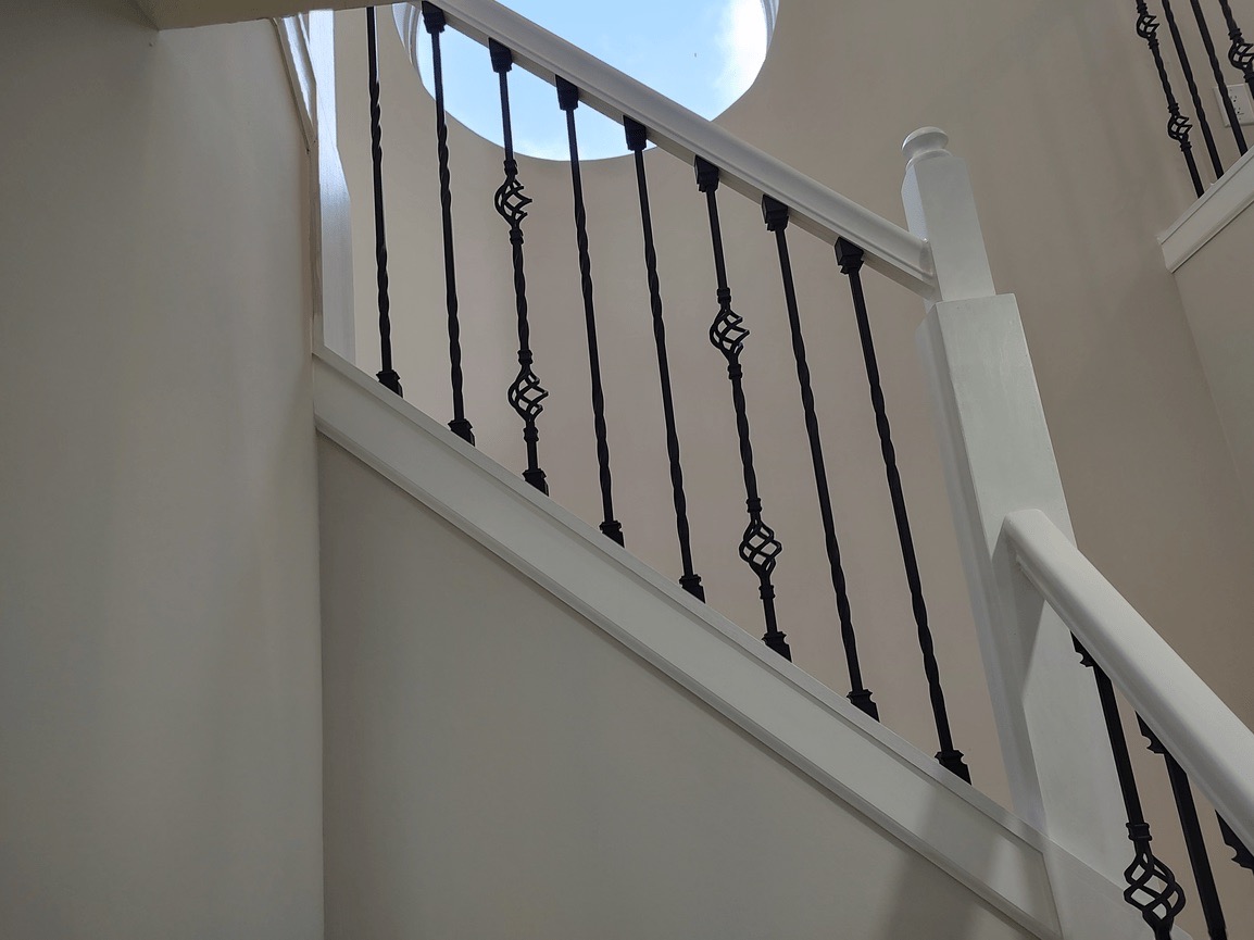 The image shows a staircase with a black railing and white steps, leading up to an open door at the top.