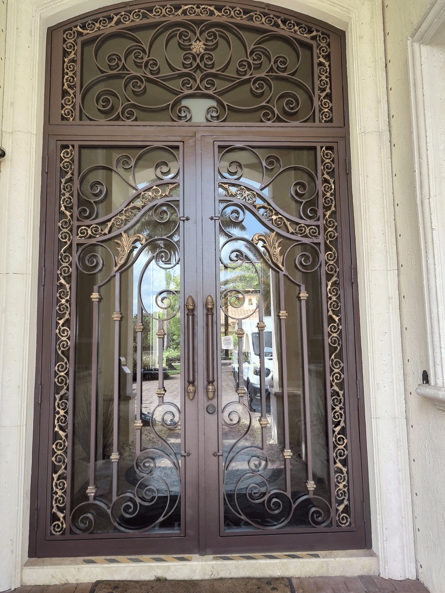 The image shows an ornate wrought iron gate with intricate scrollwork, set into a wooden door frame, leading to a building entrance.