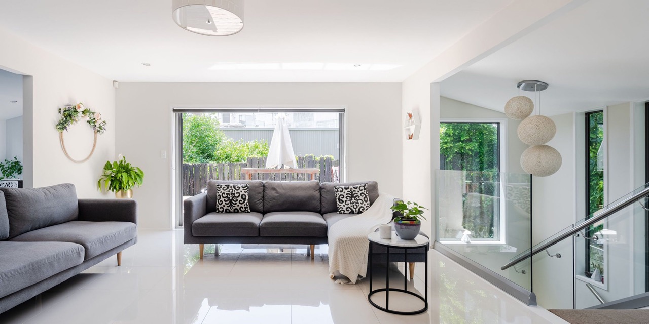 An image of a modern living room with a neutral color palette, featuring a large window, a sleek kitchen area, contemporary furniture, and a well-lit space.