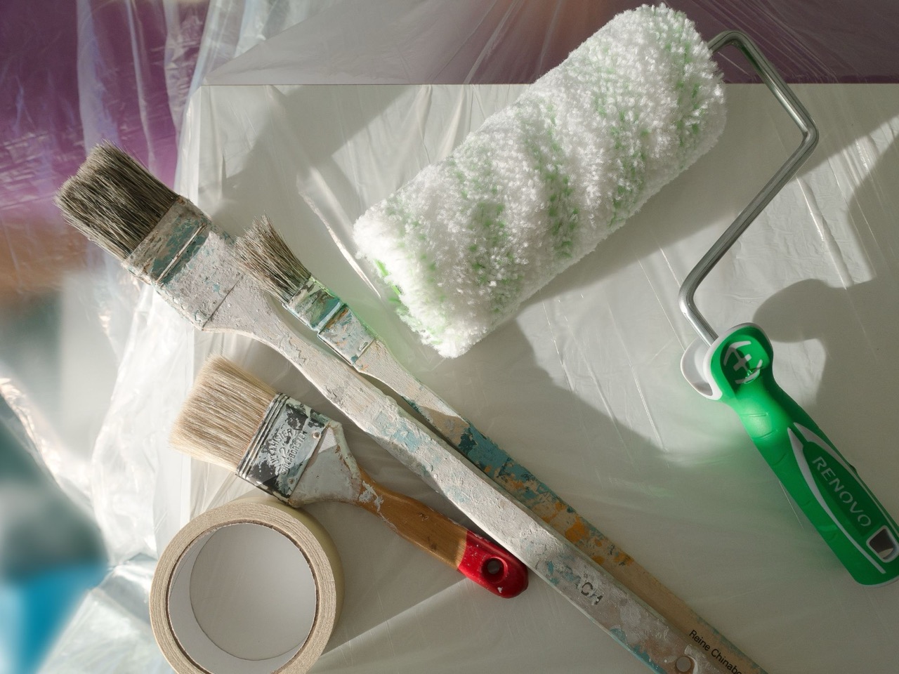 The image displays painting supplies on a surface with a green sponge and a pair of scissors, suggesting preparation for an art project or craft activity.
