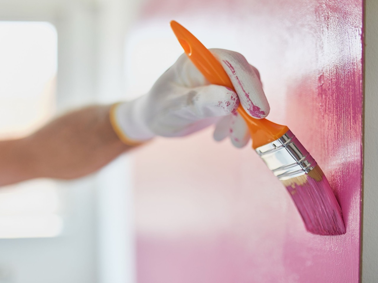 The image shows a person painting a wall with a brush, focusing on applying paint to the surface.