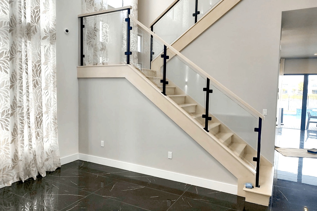 The image shows an interior view of a staircase with a modern design, featuring a glass railing and a sleek black staircase leading up to a landing.