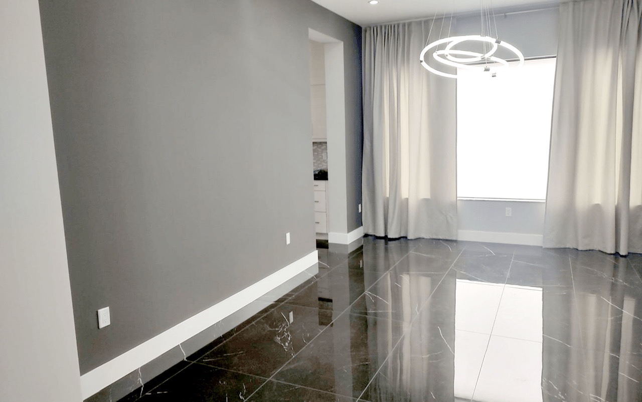 The image shows an interior view of a modern living room with a sleek design, featuring a black and white color scheme, a large window, and reflective surfaces that enhance the spaciousness of the room.