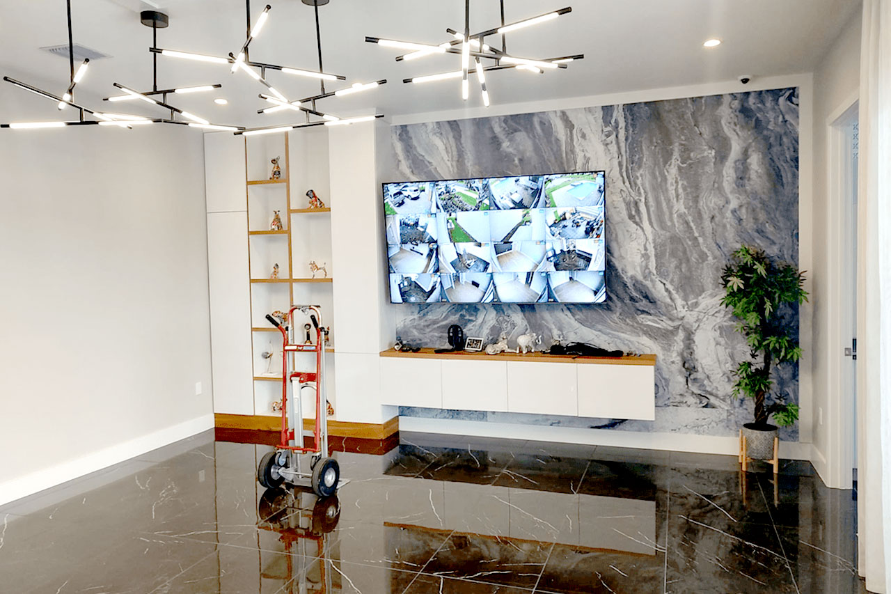 The image shows an interior space with modern design elements such as a large rock wall backdrop, a flat-screen TV displaying a nature scene, a sleek white console table, a black and white patterned floor, and a contemporary decor style.