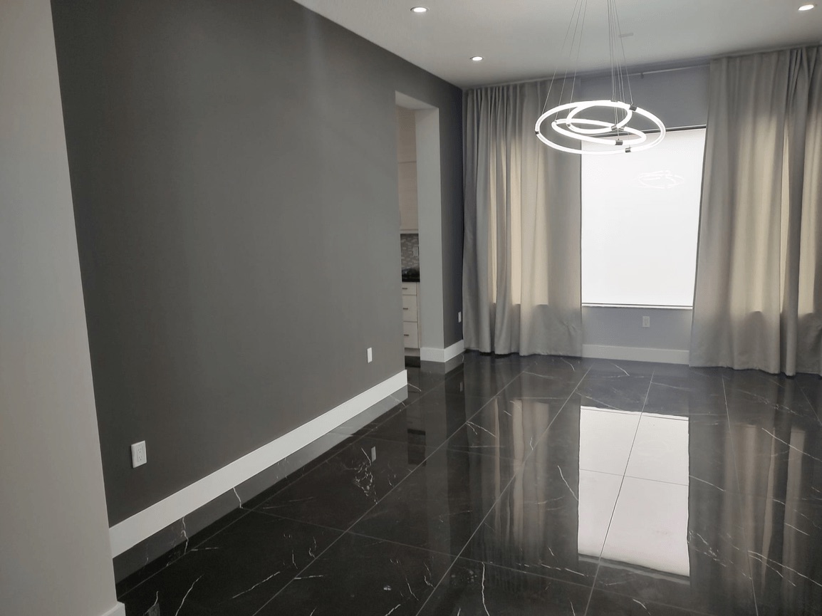 A modern interior space with a dark color scheme featuring marble flooring, a large window, and a contemporary kitchenette visible through an open doorway.