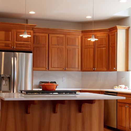 The image shows a modern kitchen interior with wooden cabinetry, stainless steel appliances, granite countertops, and a center island with a sink and stovetop.