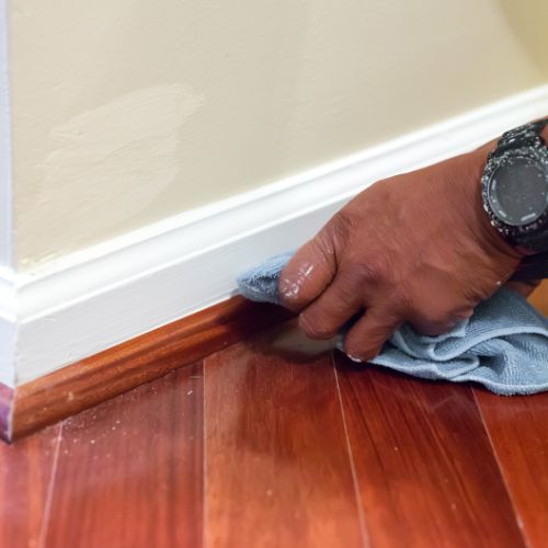 The image shows a person using a cleaning tool on a wooden floor, with a focus on the action of scrubbing a section of the floor.