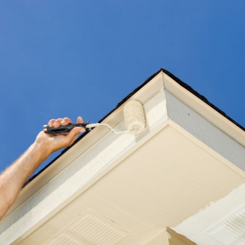 The image displays two photos side by side showing a person engaged in roofing work, with the left photo capturing the process of applying a white substance to the roof using a brush, and the right photo showing the completed roof with a neatly finished appearance.