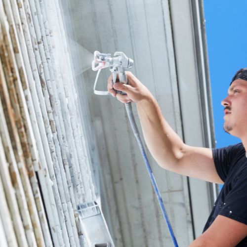 A man using a spray gun on a building.