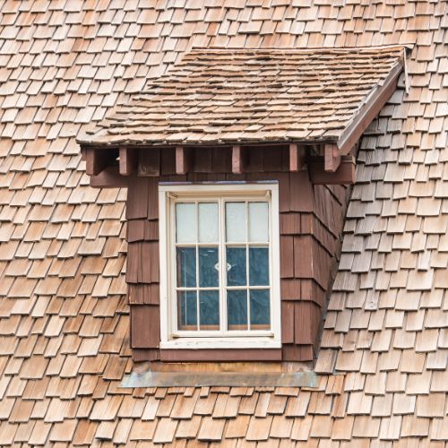 The image features a wooden window with shutters on the roof of a building, which appears to be a house with a shingled roof.