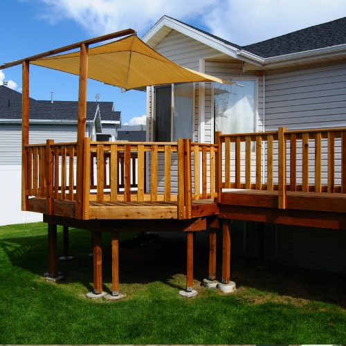The image shows an outdoor deck area with wooden railings, a pergola structure covered by a retractable awning, and a patio set on a grassy lawn. There are two different views of the same scene in the side-by-side comparison.