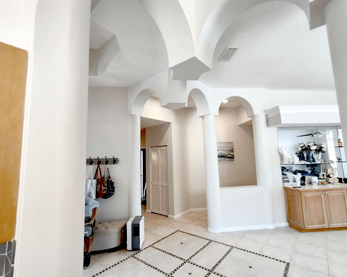 The image shows an interior view of a spacious room with high ceilings, arched doorways, and a modern architectural design featuring a combination of neutral tones and decorative elements such as light fixtures and wall art.