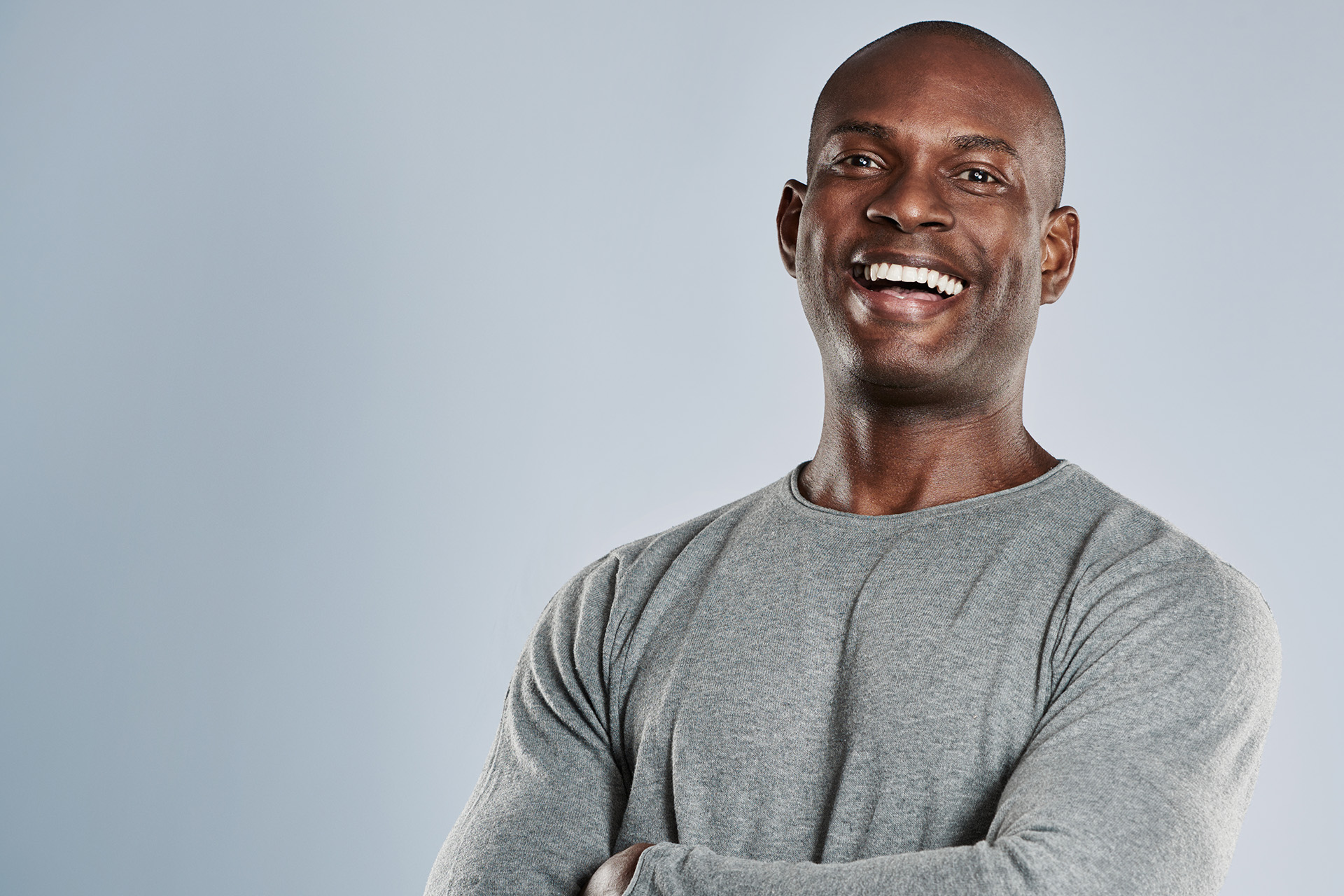 The image shows a man smiling confidently at the camera with his arms crossed.