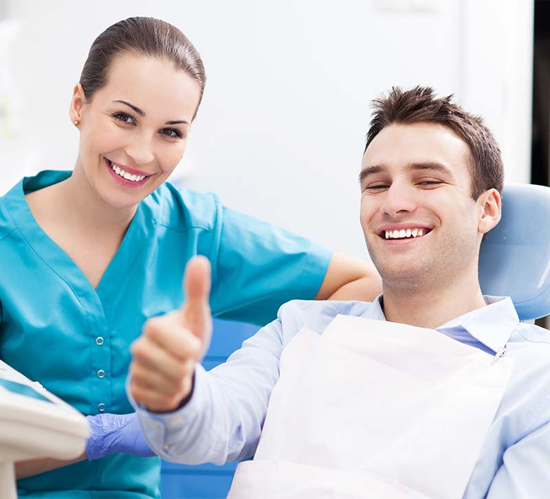 An image featuring a dental professional and a patient giving thumbs-up signs, with both smiling and appearing satisfied with their oral care experience.